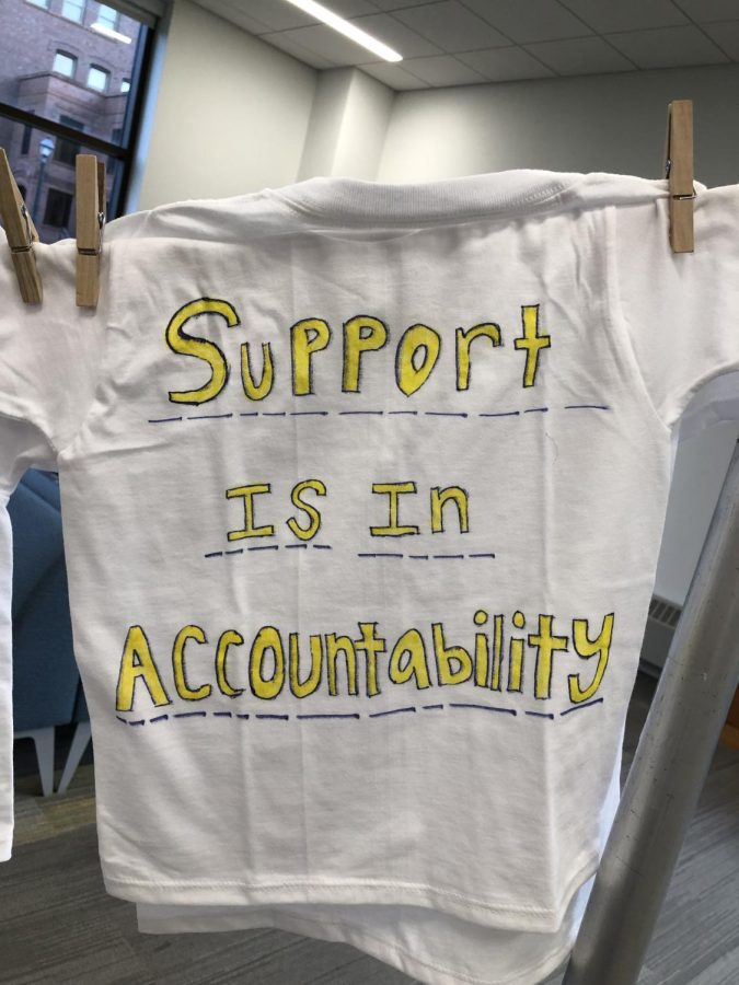 A white t-shirt with yellow writing that reads, Support is in accountability.