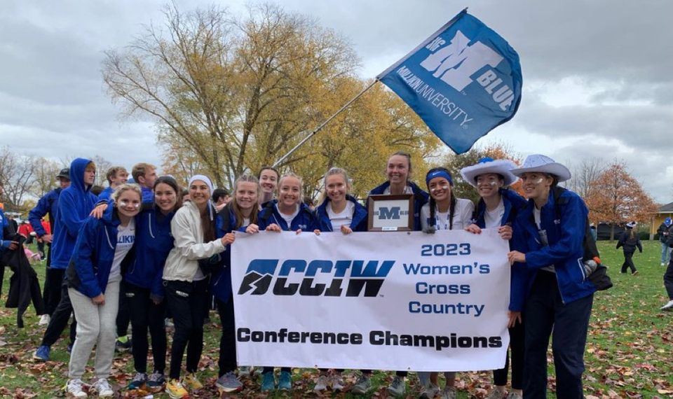 The Big Blue womens cross-country team poses for a photo with their banner. The team won their first CCIW championship in program history on Saturday.